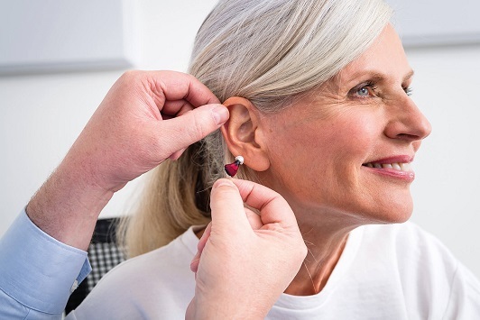 Ältere Frau bekommt ein modernes Hörgerät angepasst, Hörgeräteversorgung und Beratung.